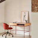 Escritorio de madera con silla roja junto a una pared blanca y viga de ladrillo