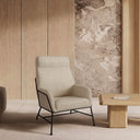Butaca MALIBÚ, en beige, en un salón con pared de mármol y banco bajo de madera