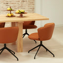 Silla tapizada ADD con pie giratorio negro, en polipiel terracota, junto a una mesa de madera – Teulat