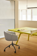 Silla de escritorio ADD con ruedas con reposabrazos, en gris claro, junto a una mesa amarilla – Teulat