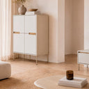 Aparador alto Bergen beige de 130 cm con 4 puertas, en un salón con cortina y alfombra de fibra