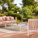 Conjunto de muebles de exterior con sofá rosa, mesa blanca y alfombra en jardín de MB Mobles