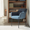 Silla SADIRA con brazos en azul petróleo, junto a una librería – Teulat